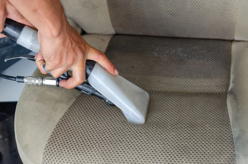 Hands using an upholstery extraction nozzle on a fabric car seat